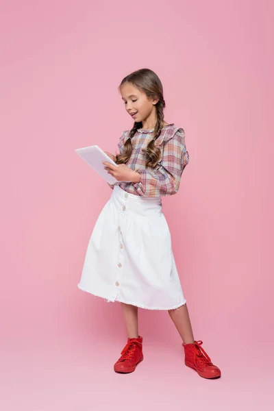 Preteen child in white skirt and plaid blouse using digital tablet on pink background — Photo de stock