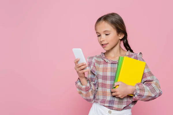 Preteen menina com livros usando telefone celular isolado em rosa — Fotografia de Stock