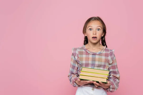 Bambino sorpreso guardando la fotocamera mentre teneva libri isolati su rosa — Foto stock