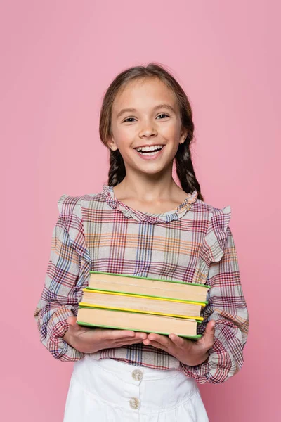 Aufgeregtes Mädchen in karierter Bluse, Bücher in der Hand und lächelnd in die Kamera, isoliert auf rosa — Stockfoto