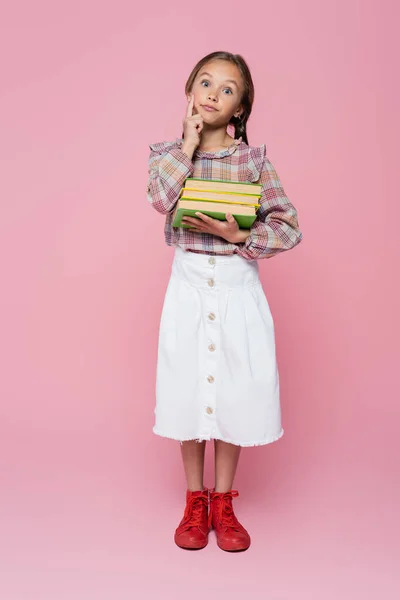 Discouraged girl in checkered blouse and white skirt holding books on pink background — Photo de stock