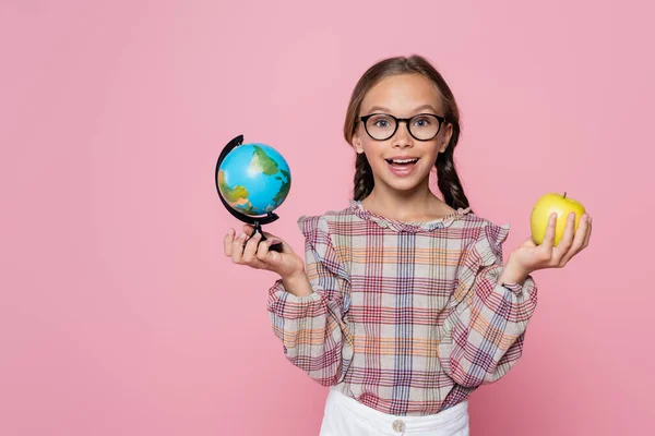 Amazed girl with green apple and small globe looking at camera isolated on pink - foto de stock