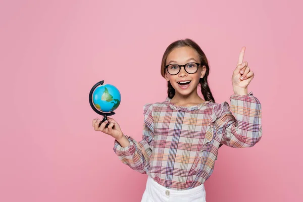 Erstaunt Mädchen mit kleinen Globus zeigt Idee Geste, während Blick in die Kamera isoliert auf rosa — Stockfoto