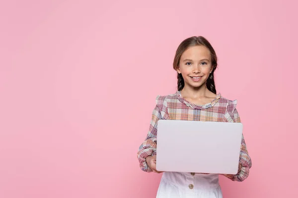 Preteen ragazza sorridente alla fotocamera, mentre tenendo il computer portatile isolato su rosa — Foto stock