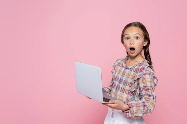 Erstaunt Mädchen mit Laptop Blick auf Kamera isoliert auf rosa — Stockfoto