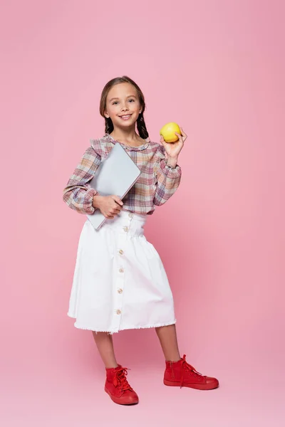 Smiling girl with laptop and green apple looking at camera on pink background - foto de stock