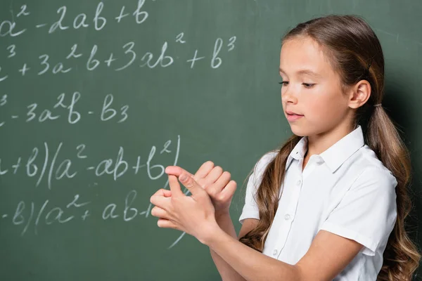 Preteen schoolgirl counting on fingers near chalkboard with mathematic equations — Photo de stock