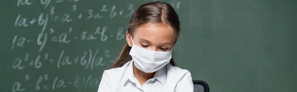 Schoolgirl in medical mask near blurred chalkboard with mathematic equations, banner — Photo de stock