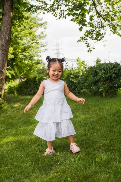 Счастливая азиатская девушка в платье стоя и улыбаясь снаружи — стоковое фото