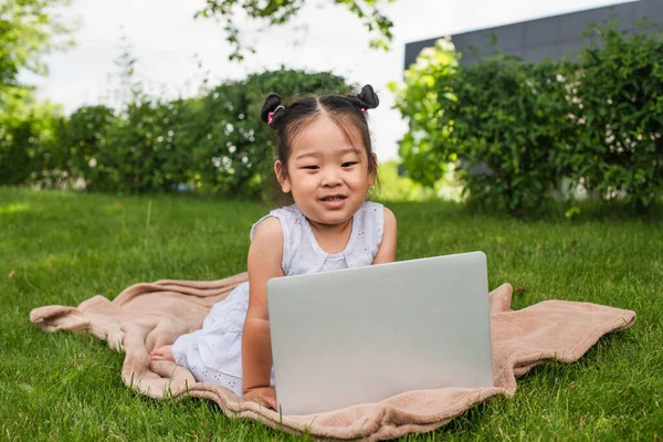 Heureux asiatique enfant regarder caméra près ordinateur portable dans parc — Photo de stock