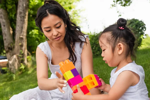 Young asian mother and blurred toddler girl playing building blocks in park — Stock Photo