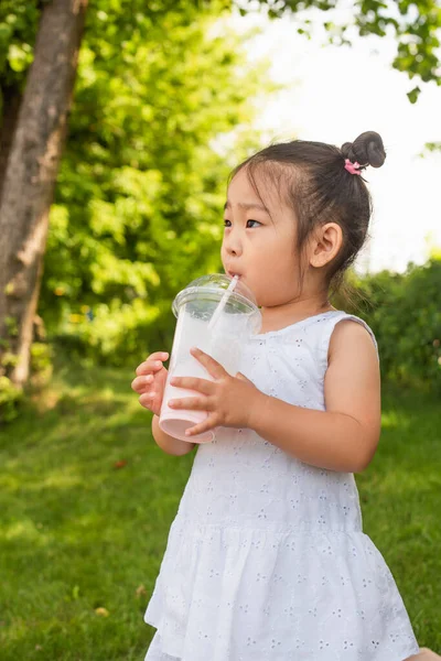 Asiatique tout-petit fille en robe boire savoureux milkshake dans parc — Photo de stock