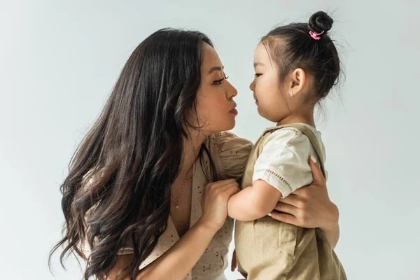 Side view of stylish asian mother hugging toddler daughter isolated on grey — Stock Photo