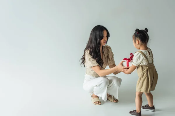 Comprimento total de elegante asiático mãe receber presente de criança filha no cinza — Fotografia de Stock