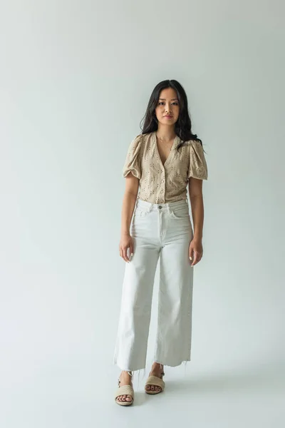 Full length of asian brunette woman in trendy outfit posing on grey — Stock Photo