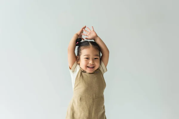 Счастливая азиатская девочка с поднятыми руками изолирована на сером — стоковое фото