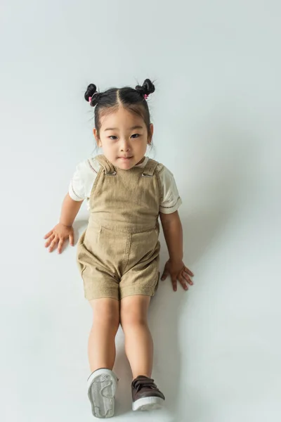 Vue grand angle de asiatique tout-petit enfant posant tout en étant assis sur gris — Photo de stock