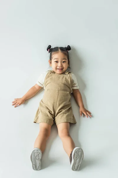 Alto ángulo vista de feliz asiático niño niña acostado en gris - foto de stock