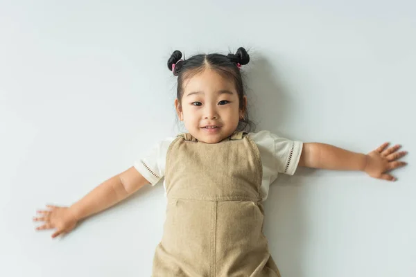 Alto angolo vista di felice asiatico bambino ragazza con le mani tese sul grigio — Foto stock