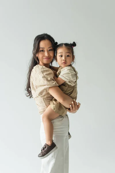 Happy asian woman holding in arms toddler daughter isolated on grey — Stock Photo