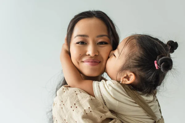 Азиатская малышка целует щеку счастливой матери, изолированной на серой — стоковое фото