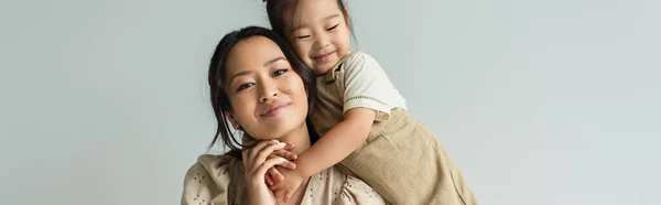 Весёлая азиатская малышка дочь обнимает счастливую мать изолированную на сером, баннер — стоковое фото