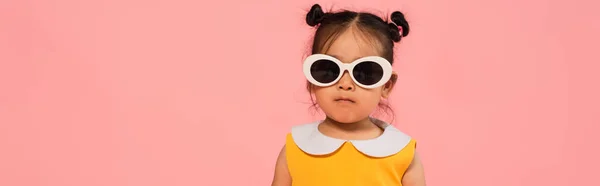 Asiatique tout-petit fille en robe et lunettes de soleil posant isolé sur rose, bannière — Photo de stock