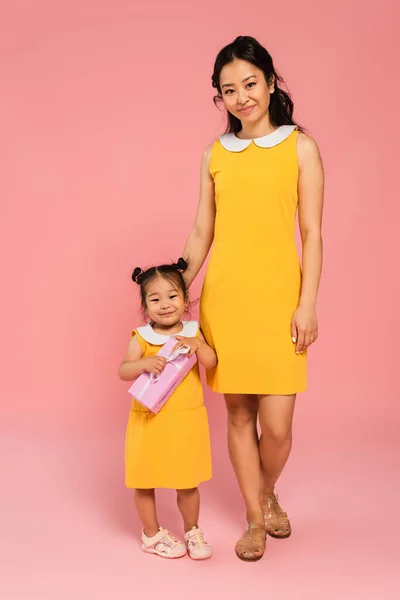 Full length of cheerful asian toddler kid holding present near mother on pink — Stock Photo