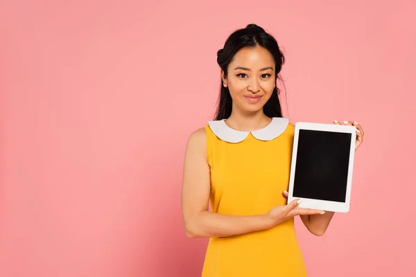 Щаслива азіатська жінка в жовтій сукні тримає цифровий планшет з порожнім екраном на рожевому — стокове фото
