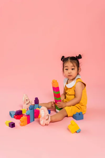 Asiatisches Kleinkind im Kleid spielt Bausteine auf rosa — Stockfoto