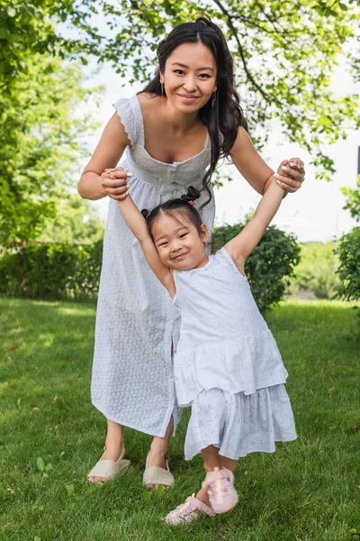 Щаслива мати і малюк азіатська дитина в сукнях тримає руки в парку — стокове фото