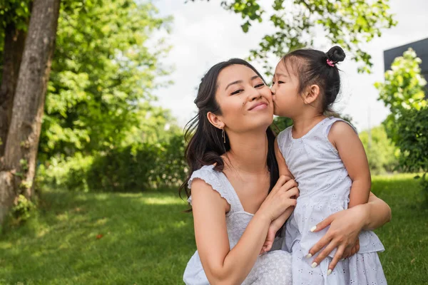 Asiático niño chica besos mejilla de feliz madre en parque - foto de stock