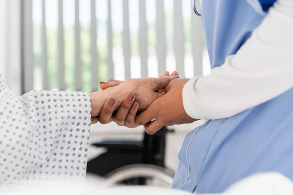 Ausgeschnittene Ansicht einer afrikanisch-amerikanischen Krankenschwester, die die Hand eines älteren Patienten hält — Stockfoto