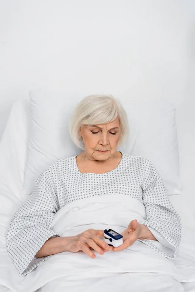 Senior patient using oximeter on bed in hospital ward — Stock Photo