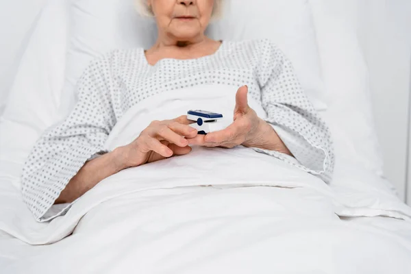 Vista ritagliata di ossimetro in mani di paziente anziano su letto di ospedale — Foto stock