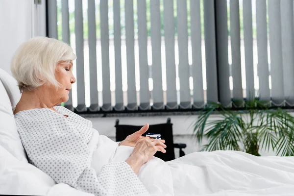 Side view of elderly patient using oximeter on hospital bed — Stock Photo