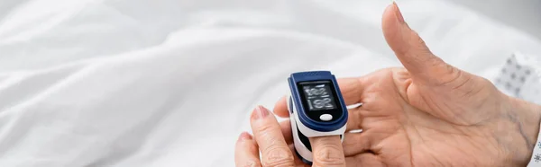 Ausgeschnittene Ansicht einer älteren Frau mit digitalem Oximeter am Krankenhausbett, Banner — Stockfoto