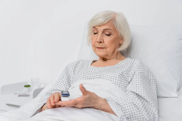 Senior woman using digital oximeter on blurred foreground in hospital — Stock Photo