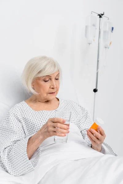 Elderly patient holding pills and glass of water in hospital ward — Stock Photo