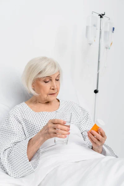 Paciente anciano sosteniendo pastillas y vaso de agua en la sala del hospital - foto de stock