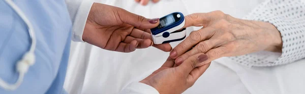 Cropped view of african american nurse fastening digital oximeter on hand of elderly patient, banner — Stock Photo