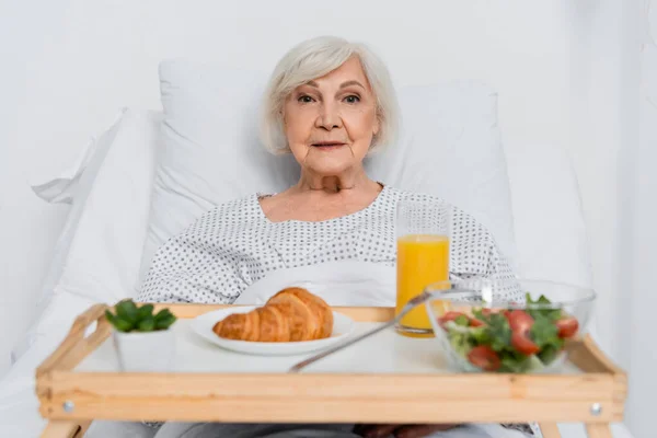 Patient âgé regardant la caméra près de la nourriture floue dans la salle d'hôpital — Photo de stock