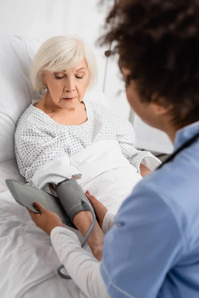 Unscharfe afrikanisch-amerikanische Krankenschwester befestigt Tonometer an Seniorin — Stockfoto