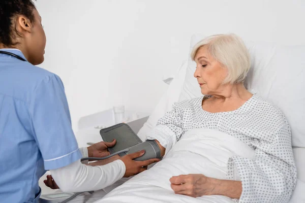 Africano americano enfermera fijación tonómetro en la mano de paciente mayor — Stock Photo