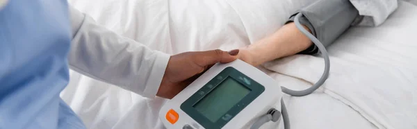 Cropped view of african american nurse holding tonometer near woman on hospital bed, banner — Stock Photo