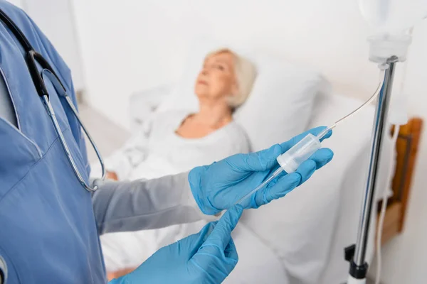 Enfermera en guantes de látex de pie cerca de la estación de terapia intravenosa en la sala de hospital - foto de stock