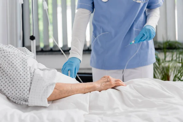 Vista recortada de la enfermera sosteniendo catéter cerca de la mujer mayor en la cama del hospital - foto de stock