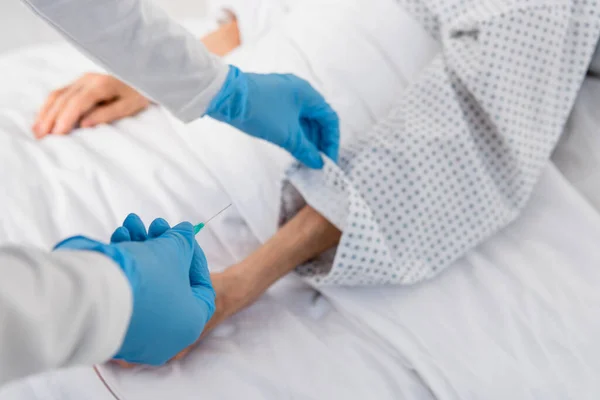 Cropped view of nurse holding needle of intravenous therapy near senior patient — Stock Photo