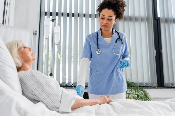 Afrikanisch-amerikanische Krankenschwester hält Katheter in der Nähe einer älteren Patientin in Klinik — Stockfoto