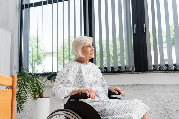 Mujer mayor en silla de ruedas mirando hacia otro lado en la sala de hospital - foto de stock